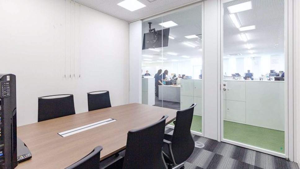 会議室の写真。ガラスの仕切りとガラスのドアがあり、椅子が5~6脚ほど向かい合って並べられている。