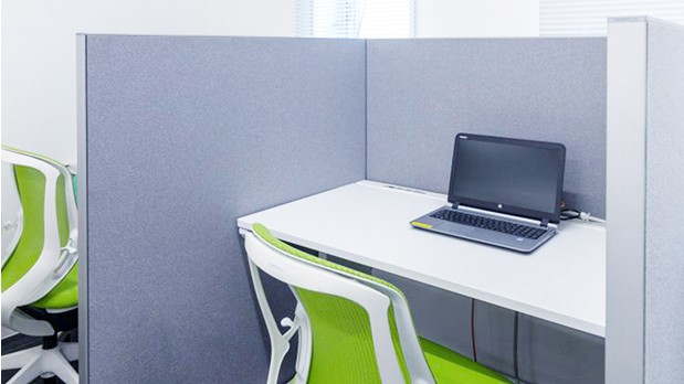 ついたてで仕切られた個室で、机と椅子がある。机の上にはノートパソコンが開いて置かれている。