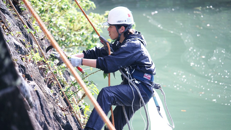  写真：ボランティアが水辺の石垣で清掃作業を行っている様子