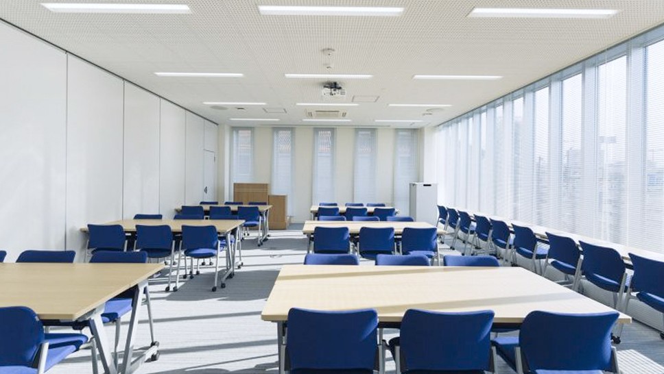 大会議室の写真。6人が向かい合わせになっているテーブルと椅子が6セット並べてあり、窓側に沿って机と椅子も設置されている。