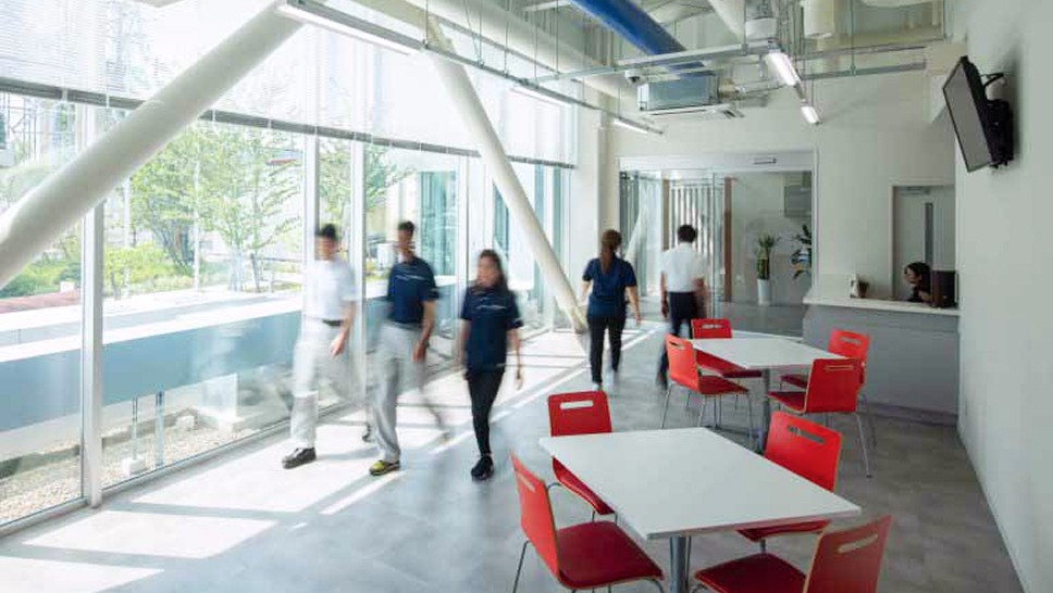 エントランスホールの画像。一面窓ガラスになっており明るい空間が広がっている。小さいテーブルと4つの椅子が並んでいる。