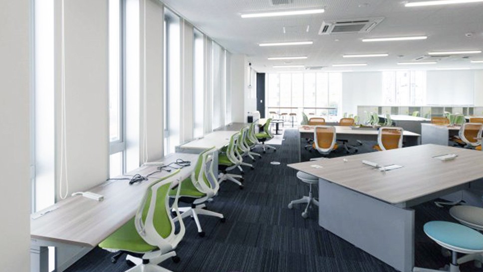 執務室の写真。机と椅子が並んでおり窓際に向かって一列に並んでいる席や、向かい合わせになっている席などいろんなスタイルのデスクが並んでいる。