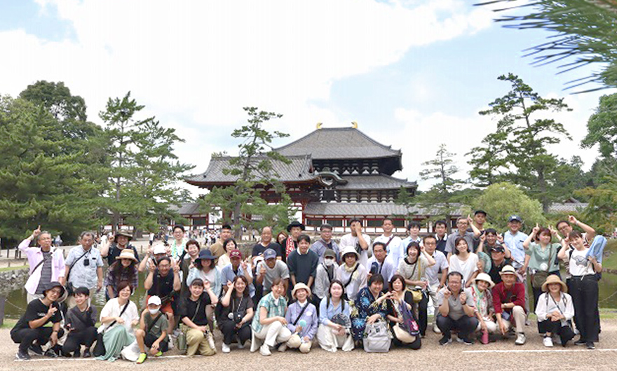 写真:オフィスで女性社員が資料を確認しながら作業し、男性社員が笑顔でサポートしている様子