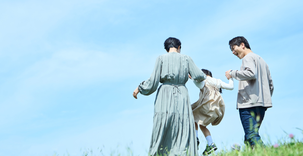 写真：青空の下、親子三人が手を繋いでいる